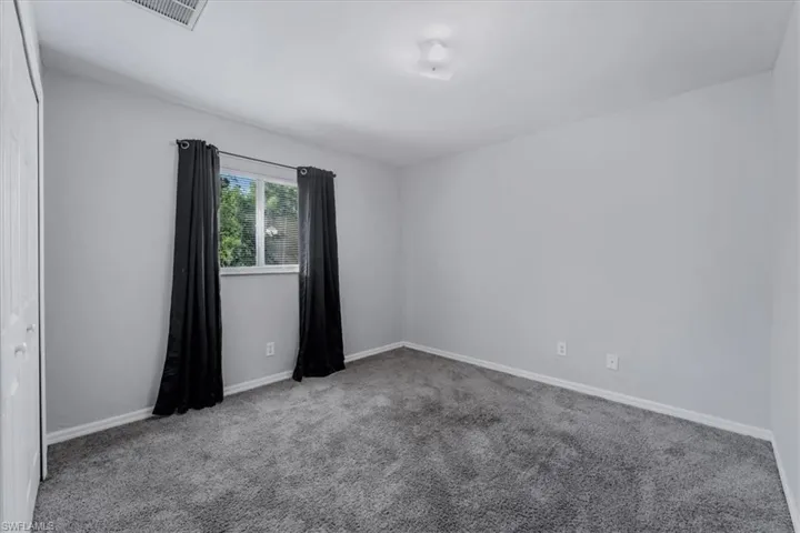 Carpeted room featuring light gray walls, a window with exterior tree views, and white baseboards