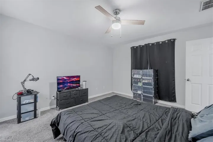 Interior room featuring light gray walls, gray carpeting, a ceiling fan with light fixture, a window with dark curtains, and a white interior door with a silver knob