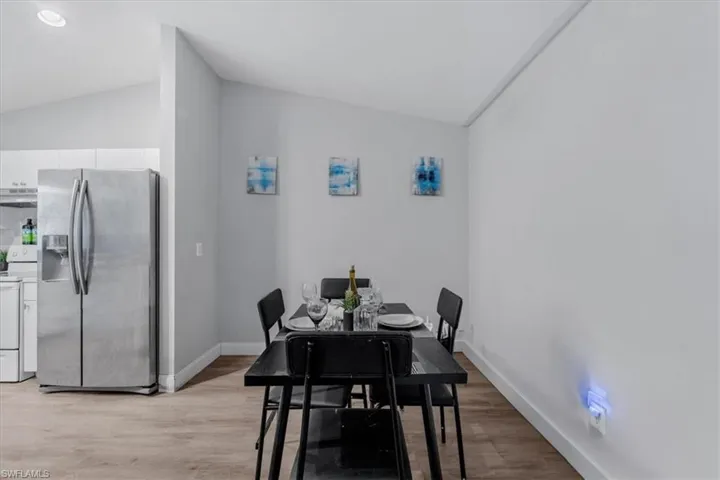 Vaulted ceiling dining area featuring wood-finish flooring, a contemporary black dining table, and a stainless steel side-by-side refrigerator
