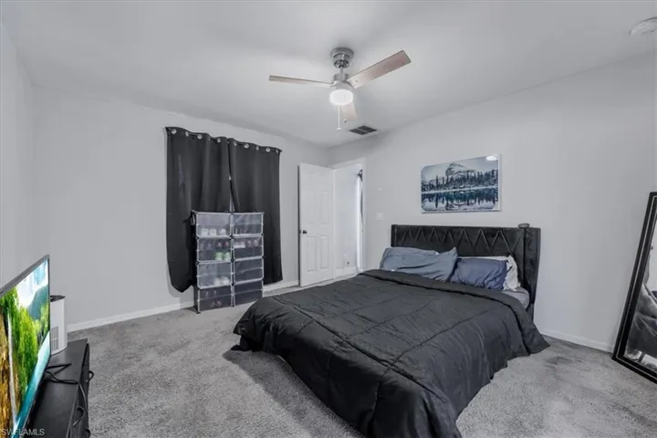 Bedroom featuring textured gray carpeting, neutral wall paint, and a ceiling fan with light fixture