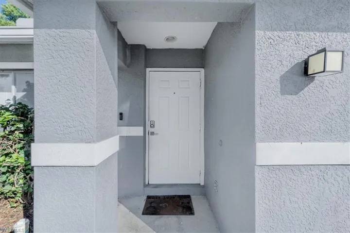 Entryway featuring a white door, textured exterior walls, an overhead recessed light, and an exterior wall-mounted light fixture