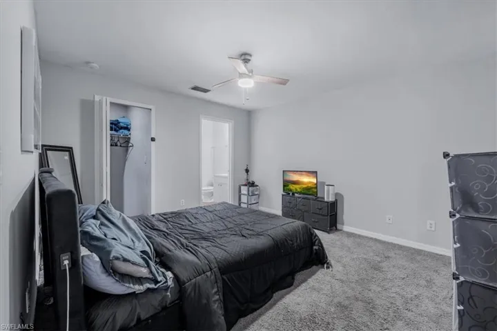Carpeted room with a ceiling fan, closet, and a doorway revealing a partial bathroom with a toilet and vanity
