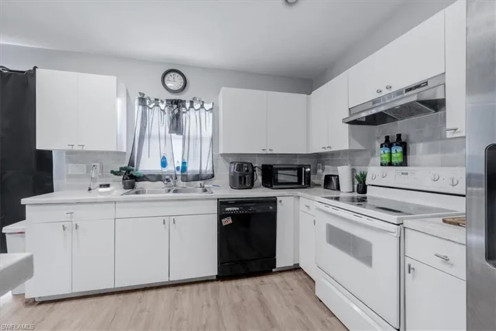 Kitchen featuring white cabinetry, light-toned countertops, tile backsplash, and wood-finish flooring