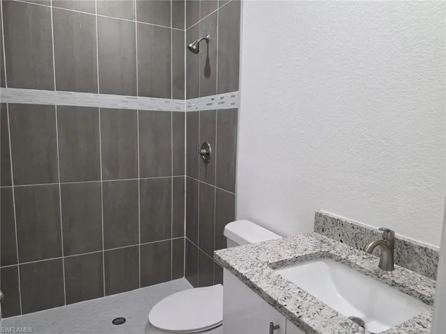 Bathroom featuring a walk-in shower with dark gray rectangular wall tiles, a decorative light-colored mosaic tile band, and a hexagonal floor tile