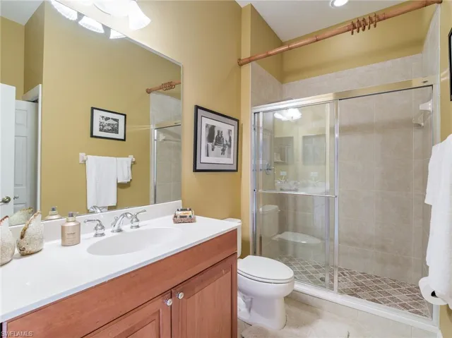 Bathroom with tile floors, a shower with door, toilet, and large vanity