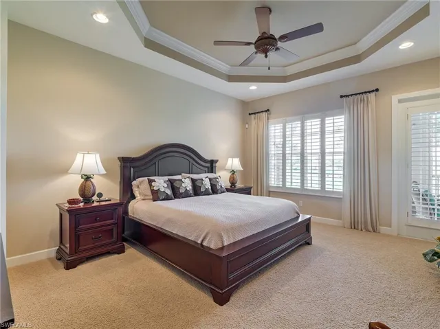 Carpeted bedroom with ceiling fan, a tray ceiling, and ornamental molding