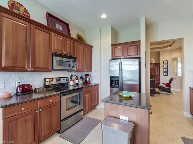Kitchen featuring a center island, light tile flooring, backsplash, and appliances with stainless steel finishes
