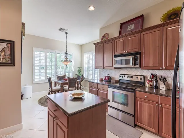 Kitchen featuring a center island, light tile floors, backsplash, and appliances with stainless steel finishes