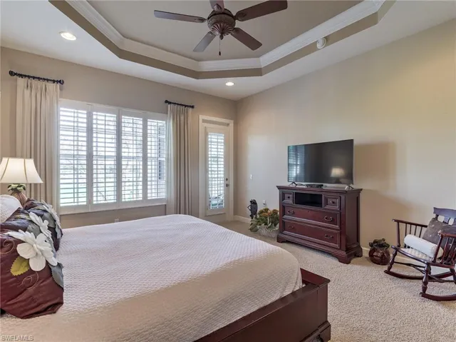 Carpeted bedroom featuring ornamental molding, ceiling fan, and a raised ceiling