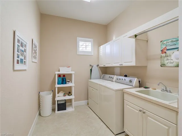 Laundry area featuring separate washer and dryer, sink, light tile flooring, and cabinets