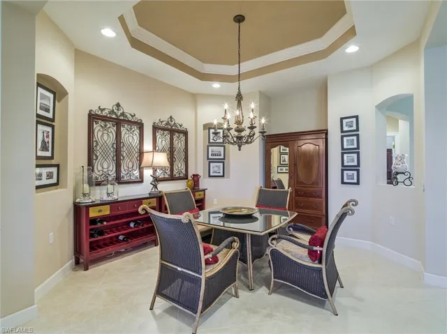 Tiled dining room featuring a notable chandelier, ornamental molding, and a tray ceiling
