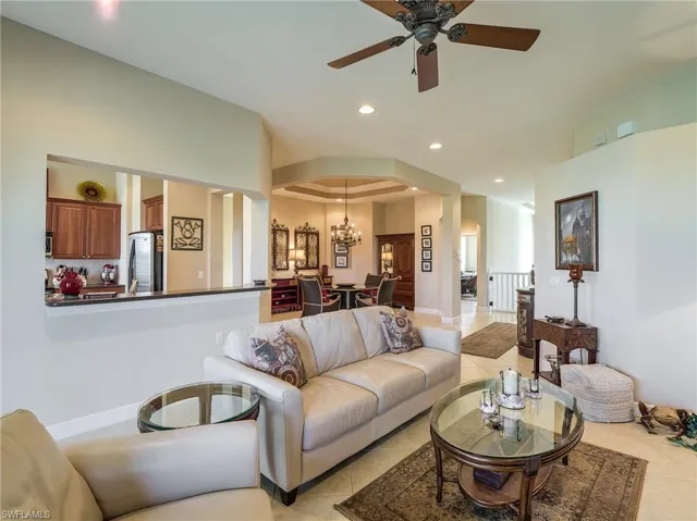 Tiled living room featuring a tray ceiling and ceiling fan with notable chandelier