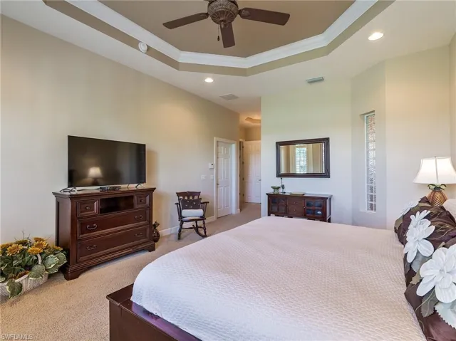 Carpeted bedroom featuring ceiling fan, a raised ceiling, and crown molding