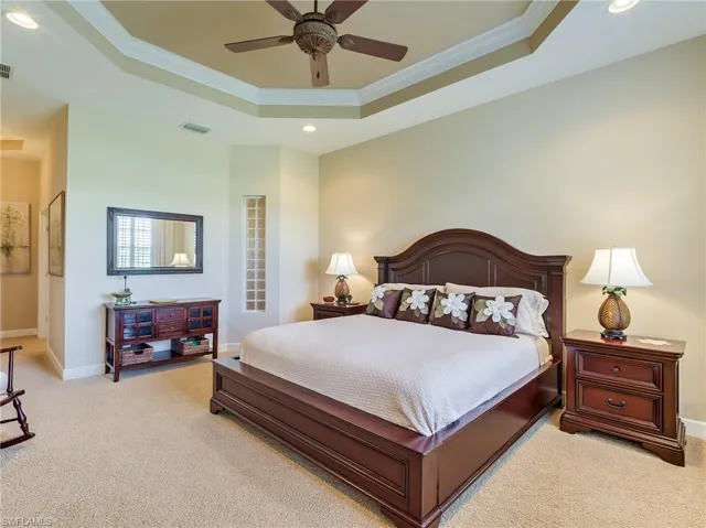 Carpeted bedroom featuring ceiling fan, a tray ceiling, and crown molding