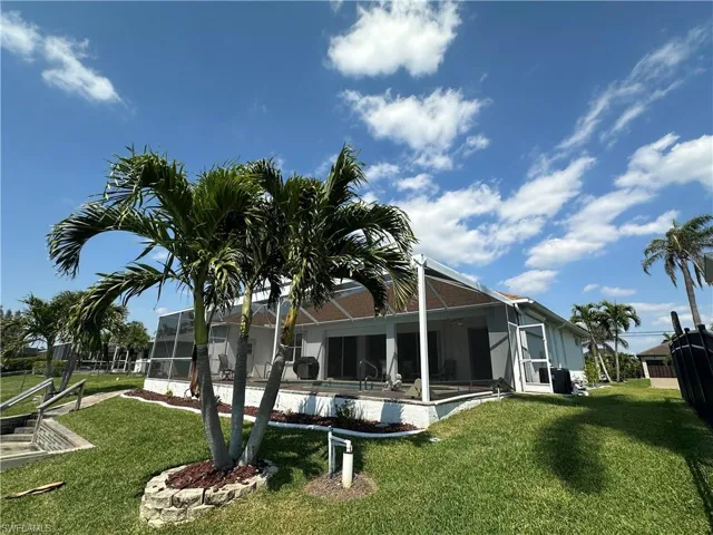 Back of property with a lawn, an outdoor pool, and glass enclosure