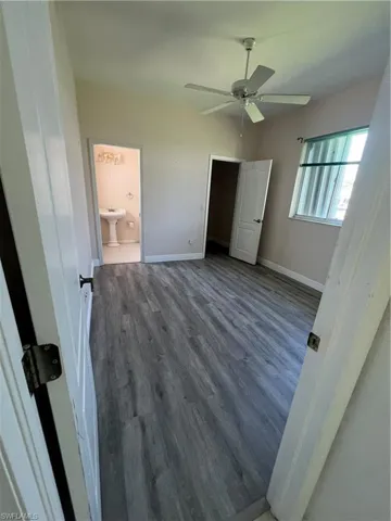 Unfurnished bedroom with wood finished floors, baseboards, a ceiling fan, and connected bathroom
