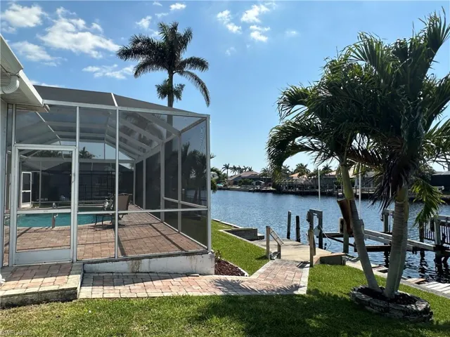 View of dock featuring glass enclosure, a water view, a patio, a yard, and an outdoor pool