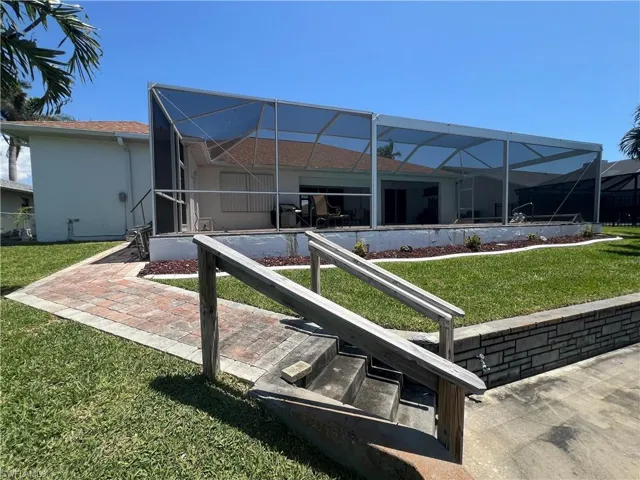 Back of house with a yard, stucco siding, and glass enclosure