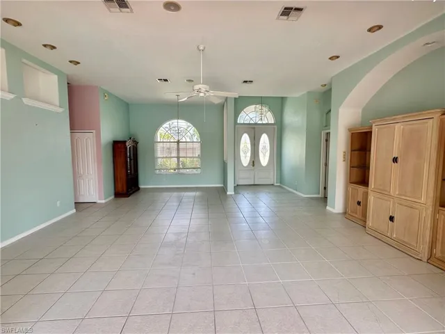Foyer featuring visible vents, a ceiling fan, light tile patterned floors, arched walkways, and baseboards