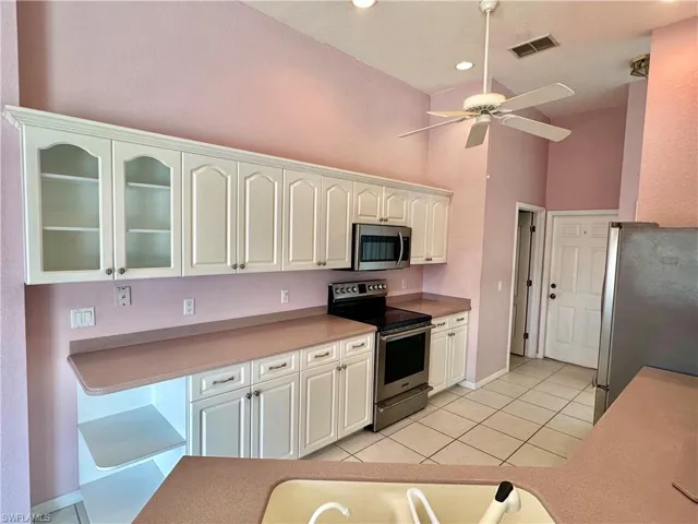 Kitchen with white cabinets, stainless steel appliances, visible vents, a ceiling fan, and light tile patterned flooring
