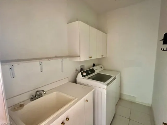 Laundry room featuring a sink, light tile patterned floors, baseboards, washer and dryer, and cabinet space