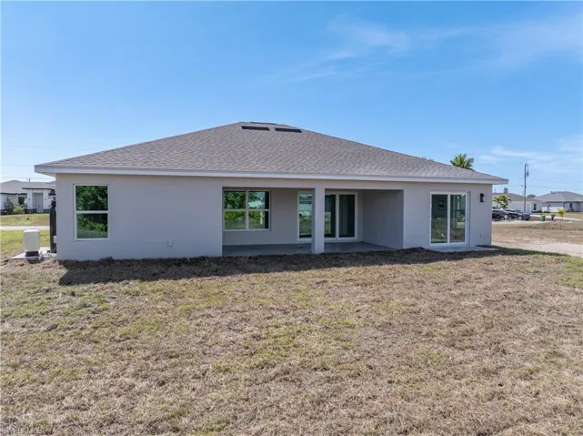 Back of property featuring a lawn, a patio area, stucco siding, and roof with shingles