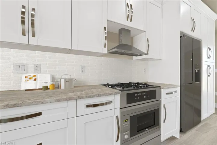 Kitchen with white cabinetry, fridge with ice dispenser, backsplash, light stone counters, and stainless steel microwave