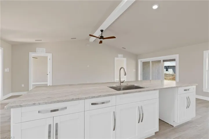 Kitchen with a ceiling fan, light stone countertops, a kitchen island with sink, light wood-type flooring, and white cabinets