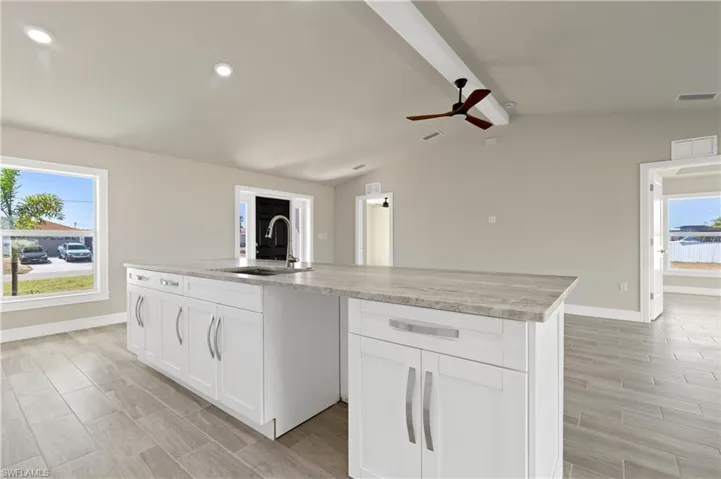 Kitchen featuring white cabinets, a ceiling fan, an island with sink, wood tiled floors, and light stone counters