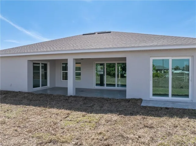Rear view of property with a patio area, stucco siding, a shingled roof, and a lawn