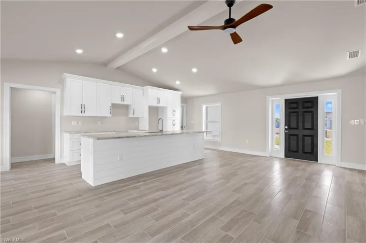 Kitchen featuring white cabinetry, a center island with sink, a ceiling fan, wood tiled floors, and light stone counters