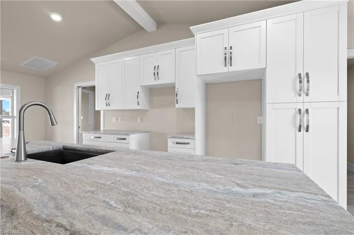 Kitchen featuring white cabinets, light stone counters, beamed ceiling, and recessed lighting