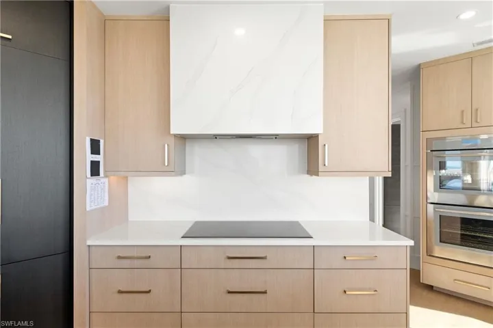 Kitchen featuring light wood finish cabinetry, stainless steel double oven, extractor fan, modern cabinets, and recessed lighting