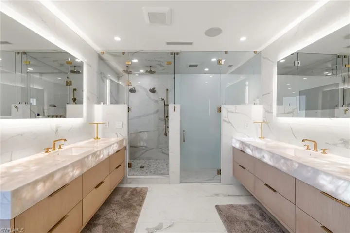 Full bath featuring two vanities, a marble finish shower, light marble finish flooring, and recessed lighting