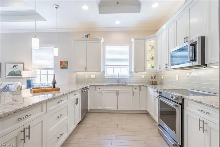 Kitchen with ornamental molding, sink, decorative light fixtures, white cabinetry, and stainless steel appliances