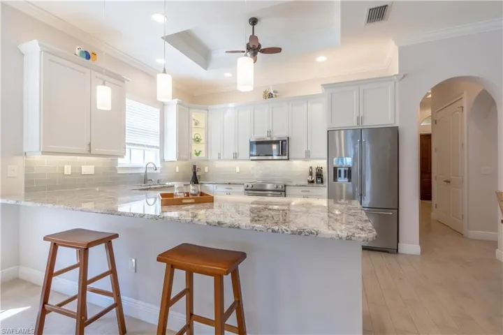 Kitchen featuring white cabinetry, kitchen peninsula, stainless steel appliances, crown molding, and ceiling fan