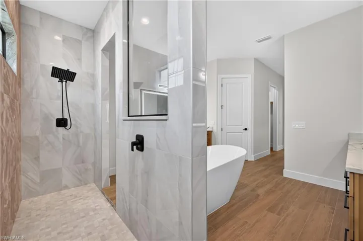 Walk-in shower with large format tile walls, black fixture finishes, and a mosaic tile floor