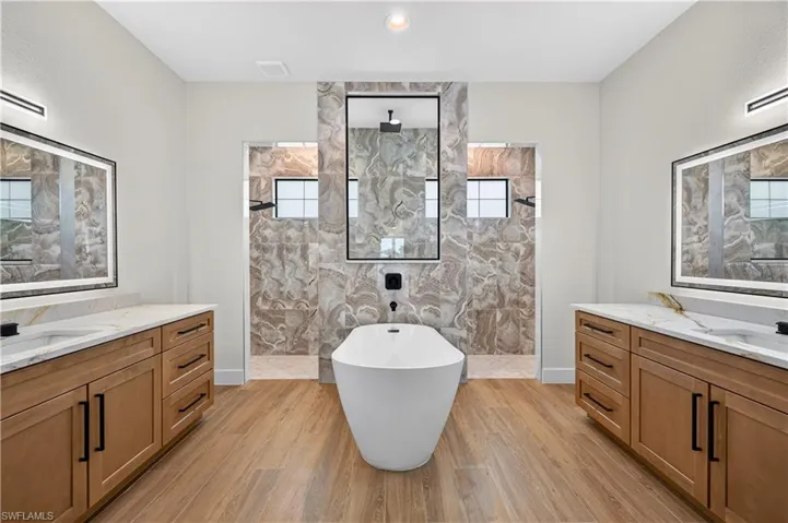Contemporary bathroom featuring a freestanding soaking tub, wood-finish flooring, and dual vanity areas with white countertops