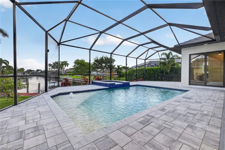 Screened outdoor living space featuring a rectangular pool with an integrated spa, a water feature, and grey paver decking