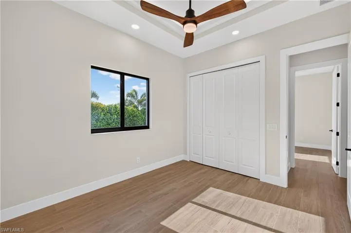 Tray ceiling featuring a modern ceiling fan, recessed lighting, and wood-finish flooring