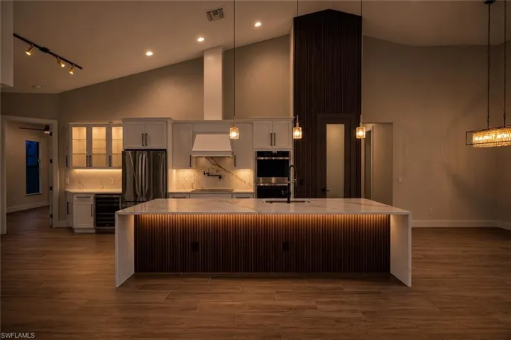 Kitchen featuring a large waterfall island with integrated lighting and a fluted wood-finish panel base