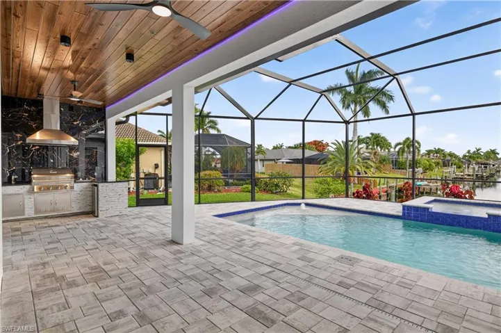 Screened outdoor living area featuring a custom pool, integrated spa, and a built-in outdoor kitchen
