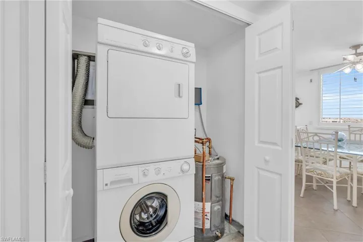 Laundry room featuring stacked washer / drying machine, ceiling fan, light tile patterned floors, and water heater, virtually enhanced image