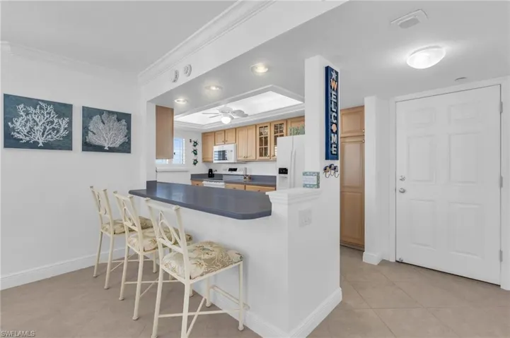 Kitchen with kitchen peninsula, a kitchen breakfast bar, ornamental molding, white appliances, and ceiling fan, virtually enhanced image