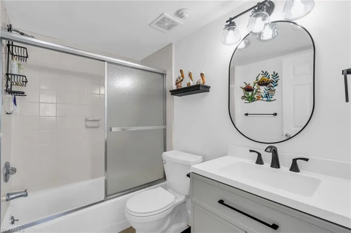 Full bathroom featuring vanity, enclosed tub / shower combo, and toilet, virtually enhanced image