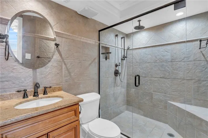 Bathroom featuring crown molding, an enclosed shower, toilet, vanity, and tile walls