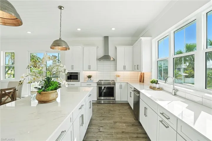 Kitchen featuring appliances with stainless steel finishes, wall chimney range hood, backsplash, light stone counters, and white cabinets