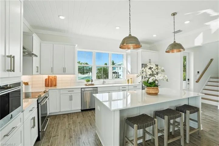 Kitchen featuring stainless steel appliances, wood finished floors, a kitchen bar, tasteful backsplash, and light countertops