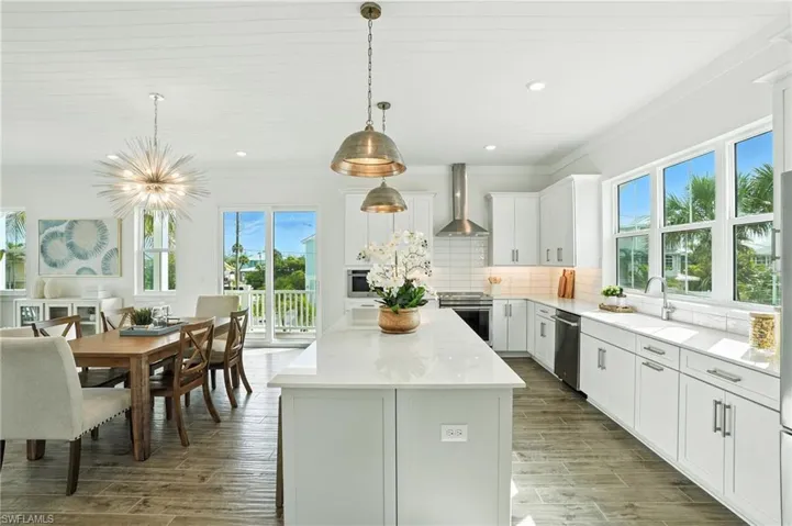 Kitchen featuring wall chimney range hood, stainless steel appliances, a kitchen island, light countertops, and decorative backsplash
