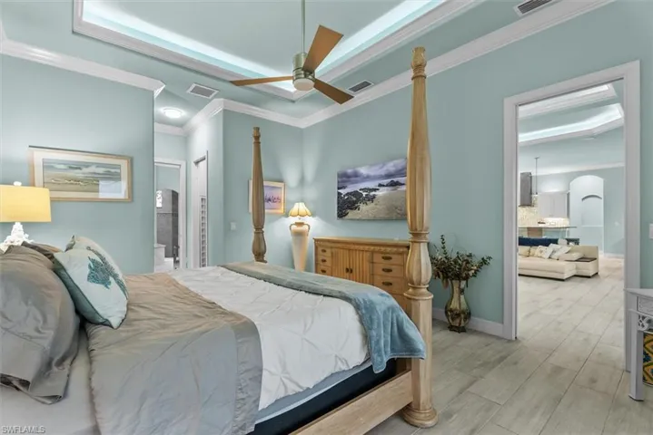 Bedroom with tray ceiling, crown molding, a ceiling fan, and light wood-finish flooring